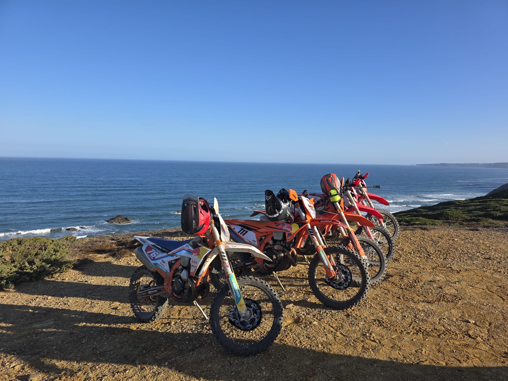 A line of KTM enduro bikes parked on a coastal trail