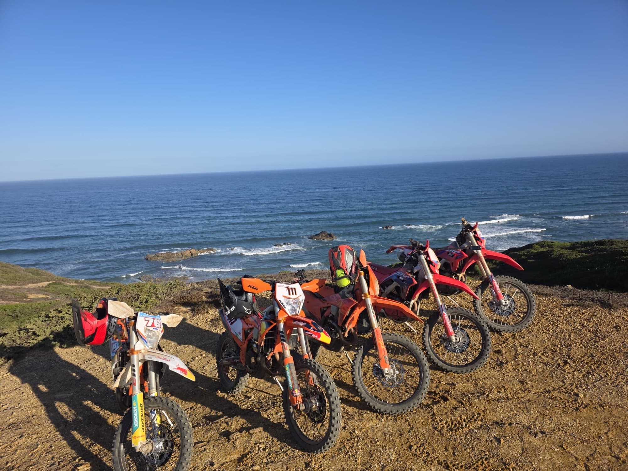 Four KTM enduro bikes parked on a clifftop overlooking the ocean