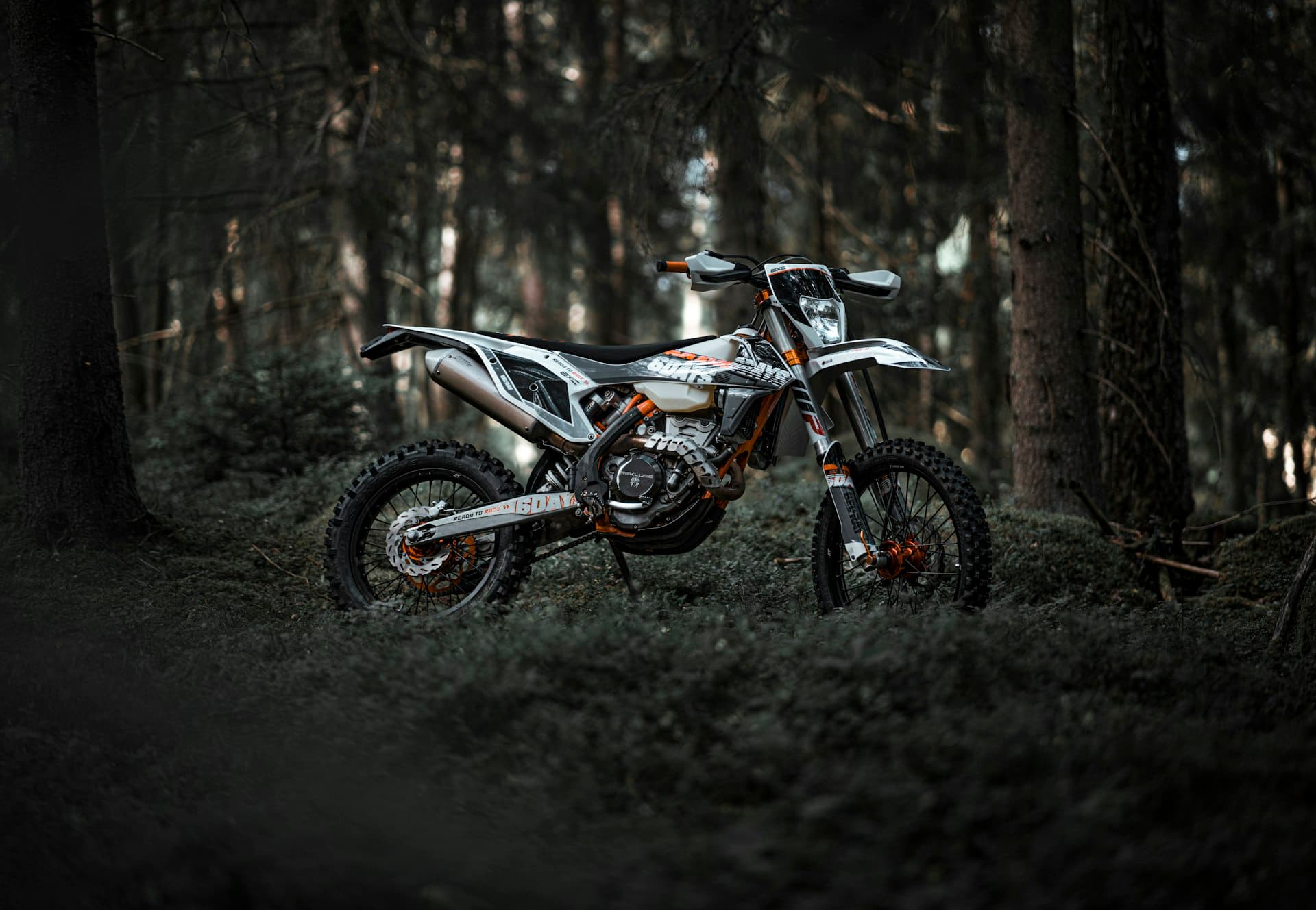 White and orange KTM enduro bike parked in a dark woodland setting