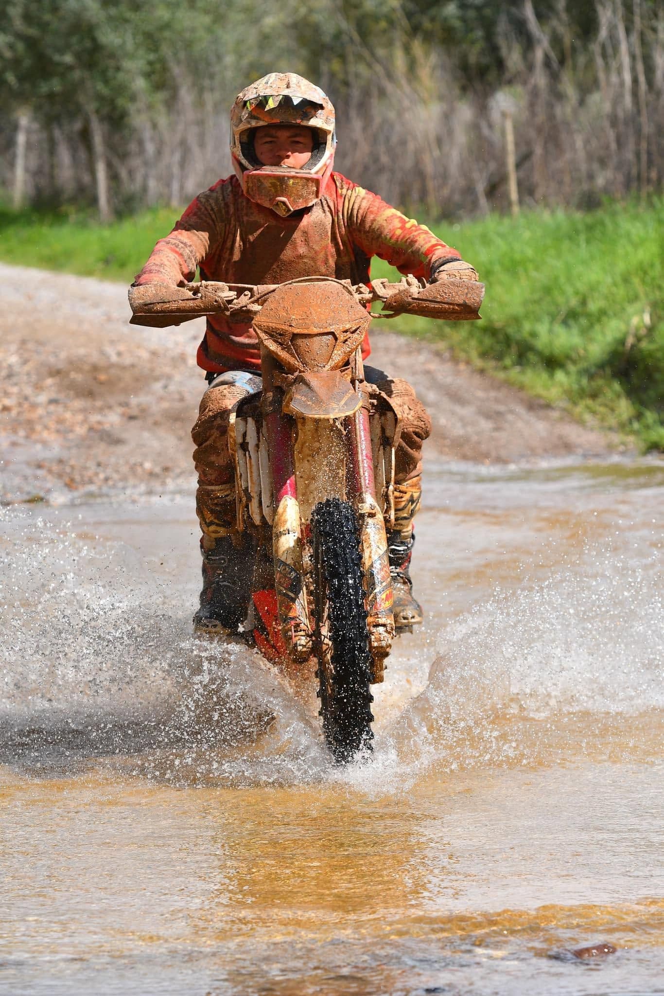 Mud-covered enduro rider charging through a water crossing on an Algarve trail