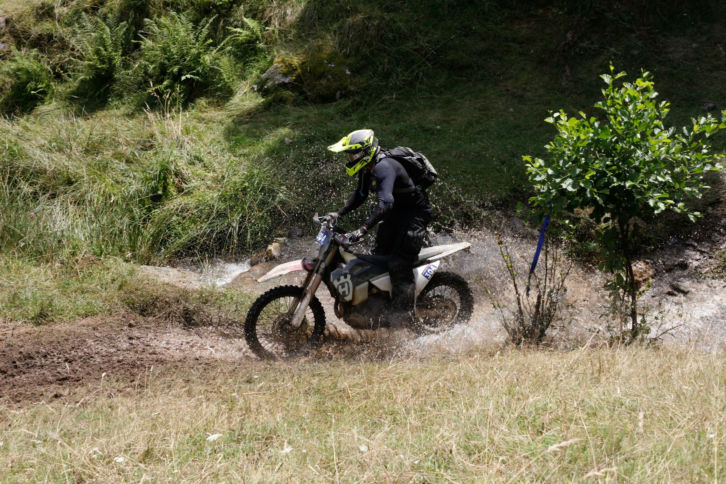 Enduro rider splashing through a muddy hillside stream