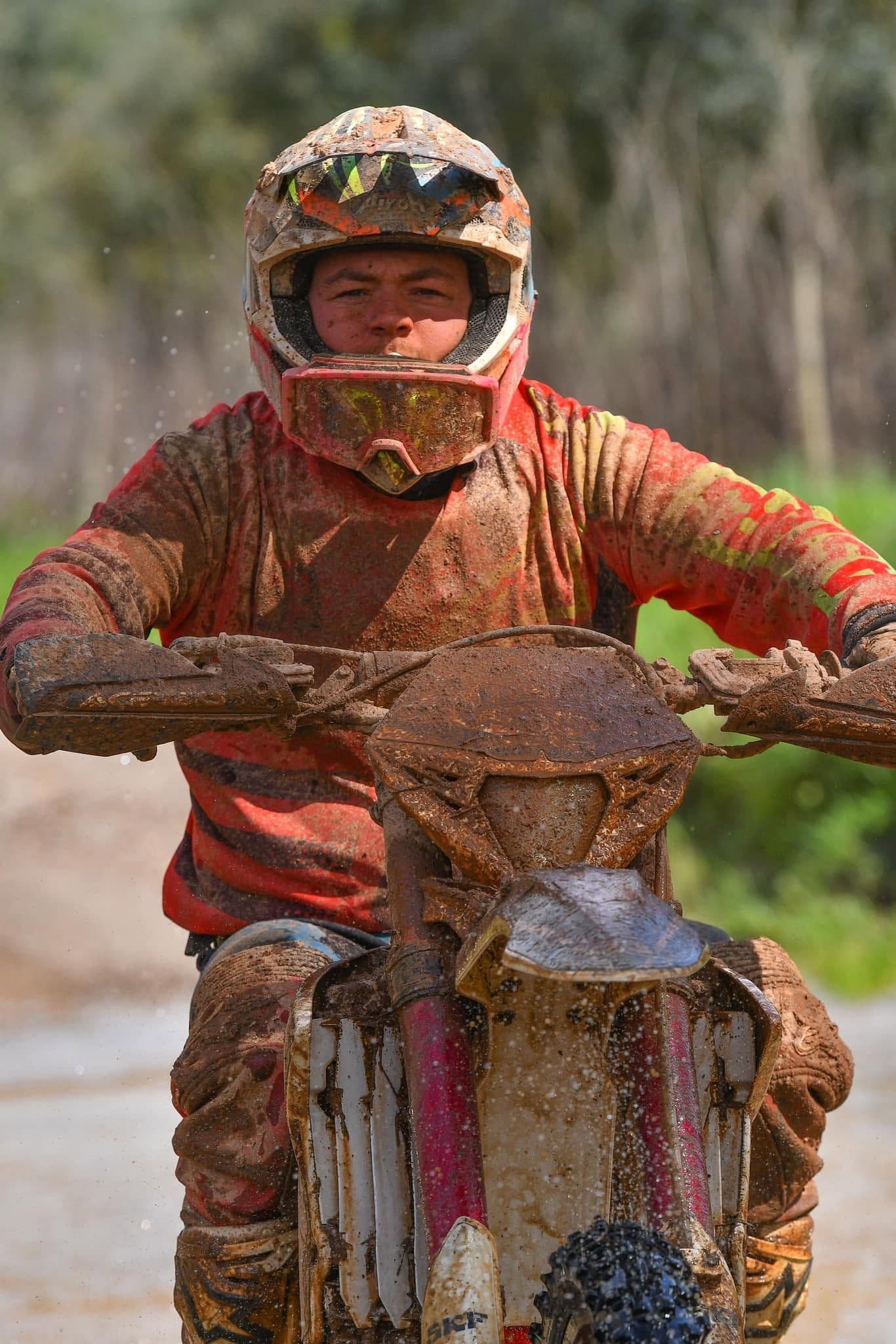 Mud-covered enduro rider charging through a trail water crossing